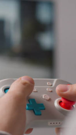 Vertical-Video-Close-Up-Hands-Man-Playing-Video-Game-Controller-Screen-In-Background